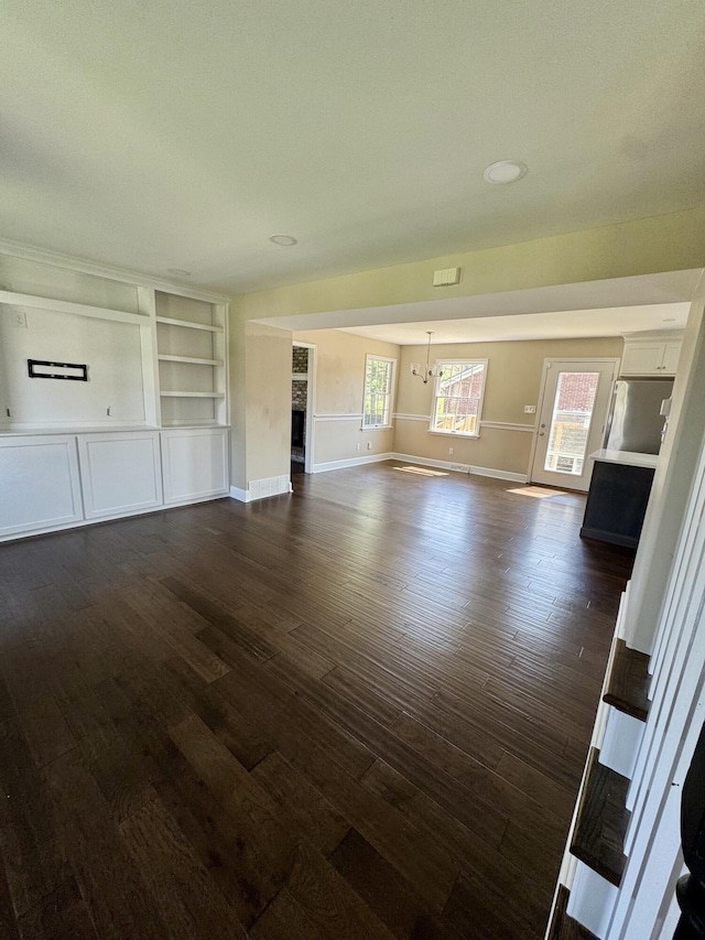 unfurnished living room with dark wood-type flooring, an inviting chandelier, and baseboards