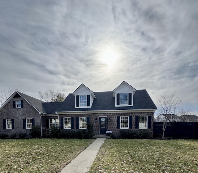 cape cod-style house featuring roof with shingles, a front yard, fence, and brick siding