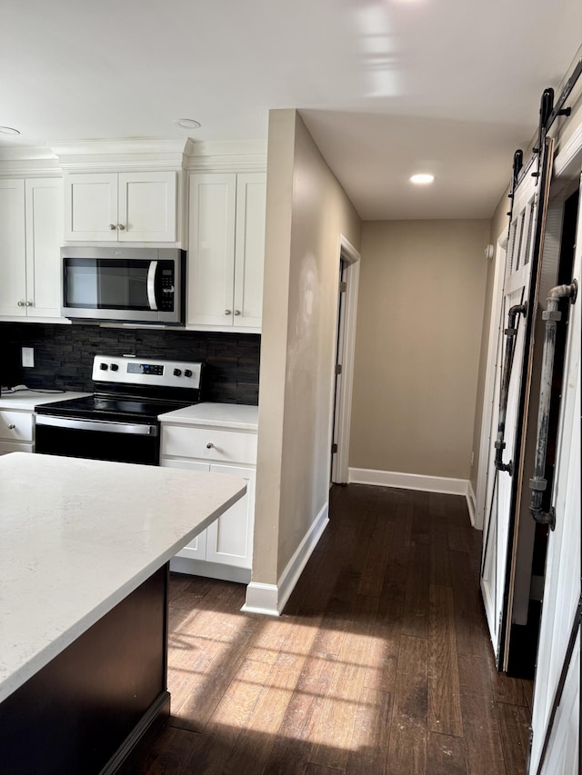 kitchen with a barn door, white cabinetry, light countertops, appliances with stainless steel finishes, and backsplash