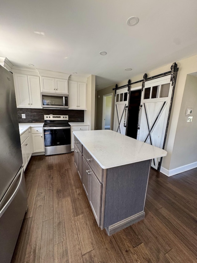 kitchen featuring stainless steel appliances, dark wood-type flooring, a barn door, and white cabinets