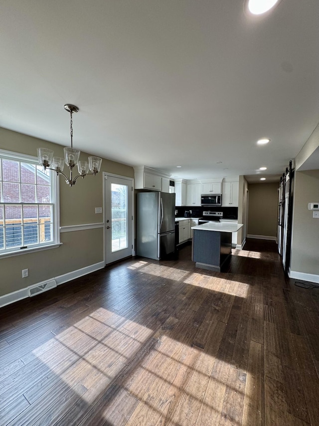 kitchen with decorative light fixtures, a center island, stainless steel appliances, light countertops, and white cabinetry