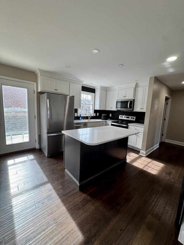 kitchen with stainless steel appliances, dark wood-type flooring, a kitchen island, white cabinetry, and light countertops