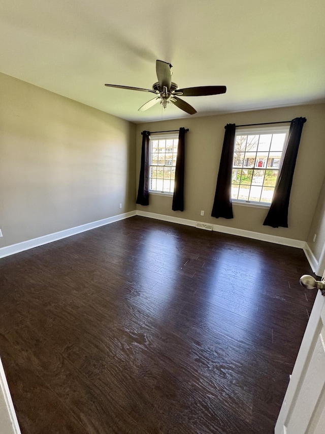 empty room with dark wood-style flooring, baseboards, a ceiling fan, and visible vents