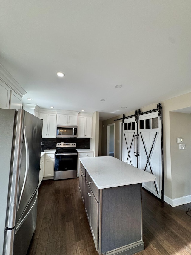 kitchen featuring a barn door, dark wood-type flooring, stainless steel appliances, light countertops, and white cabinetry