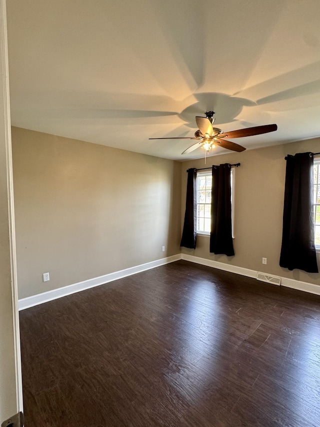 unfurnished room featuring dark wood-style floors, visible vents, baseboards, and a ceiling fan