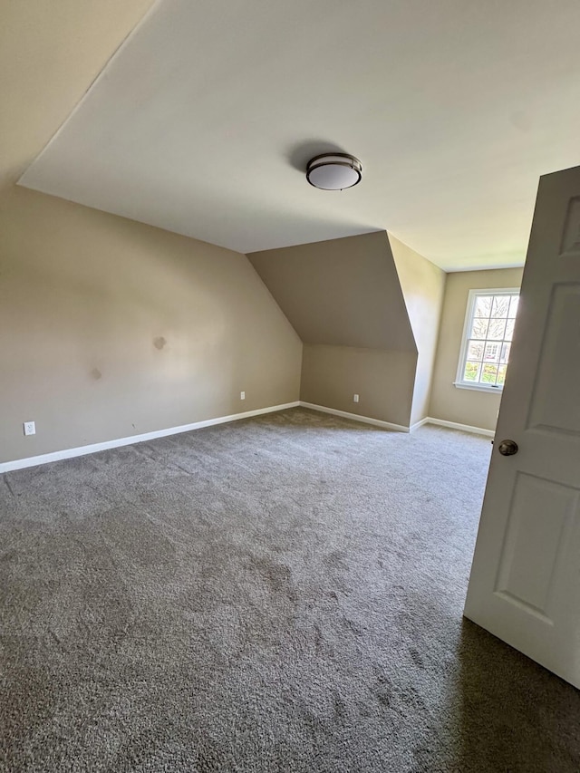 additional living space featuring dark colored carpet, lofted ceiling, and baseboards