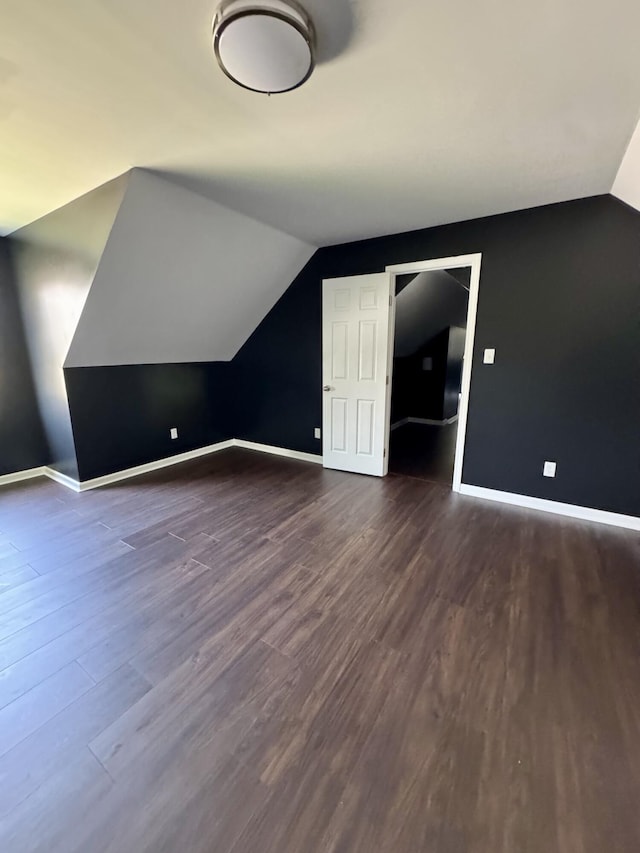 additional living space featuring dark wood-type flooring, baseboards, and vaulted ceiling