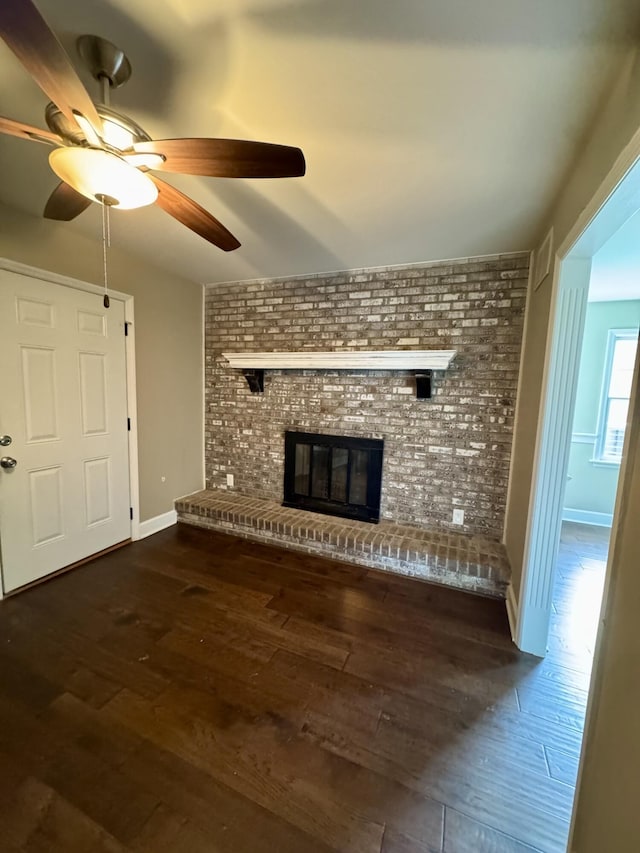 unfurnished living room with dark wood-style floors, a brick fireplace, baseboards, and brick wall