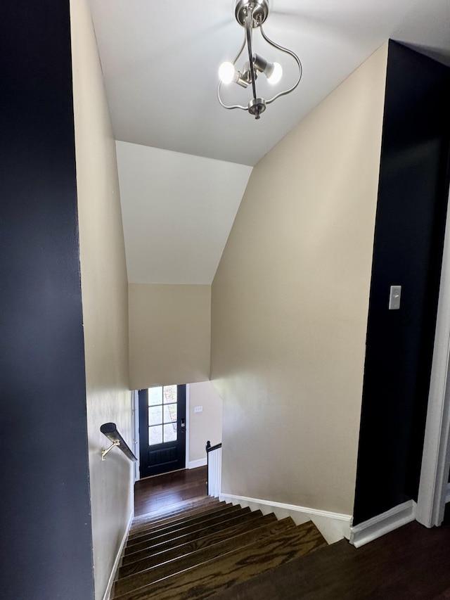 stairway featuring lofted ceiling, baseboards, an inviting chandelier, and wood finished floors