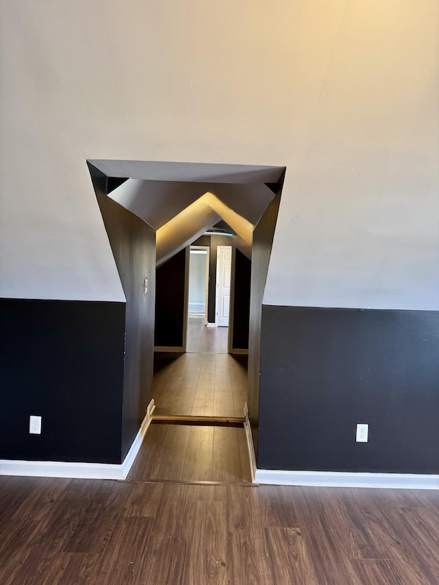 hallway featuring lofted ceiling, baseboards, and wood finished floors