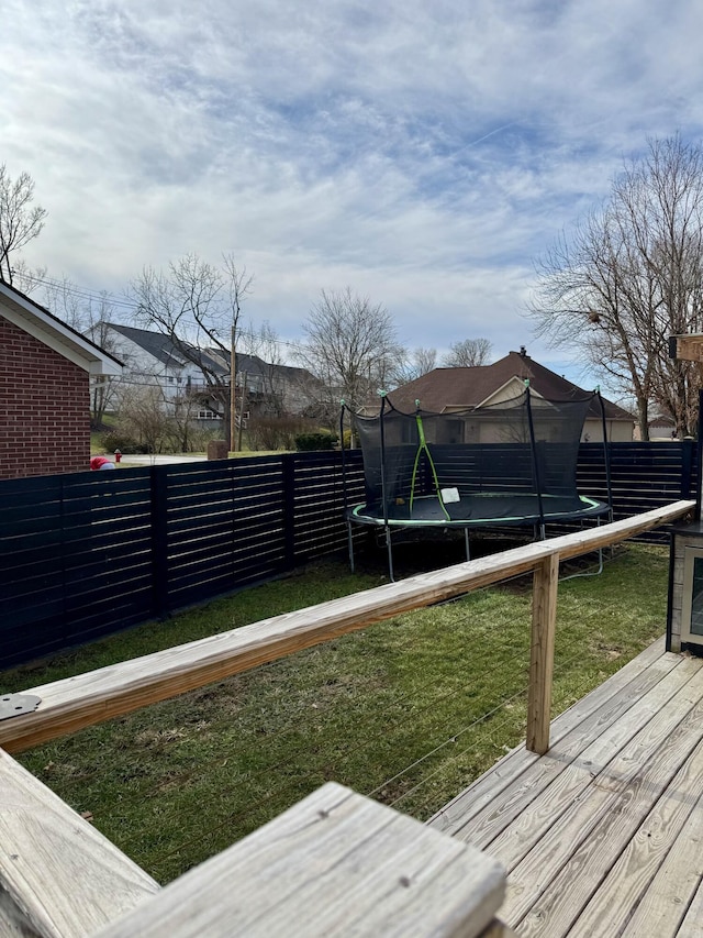 wooden deck featuring a fenced backyard, a trampoline, and a lawn