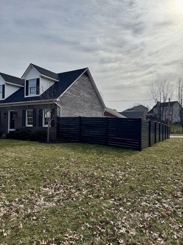 view of side of property with brick siding, a lawn, and fence