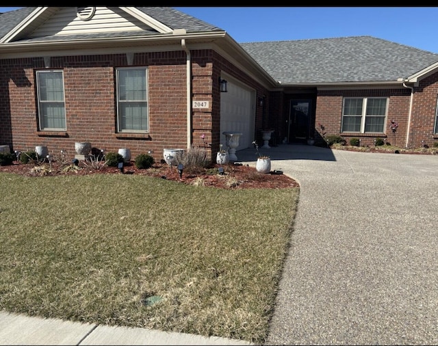 single story home with an attached garage, brick siding, driveway, roof with shingles, and a front yard