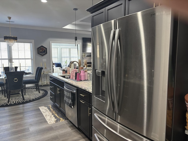 kitchen with wood finished floors, appliances with stainless steel finishes, ornamental molding, a sink, and light stone countertops