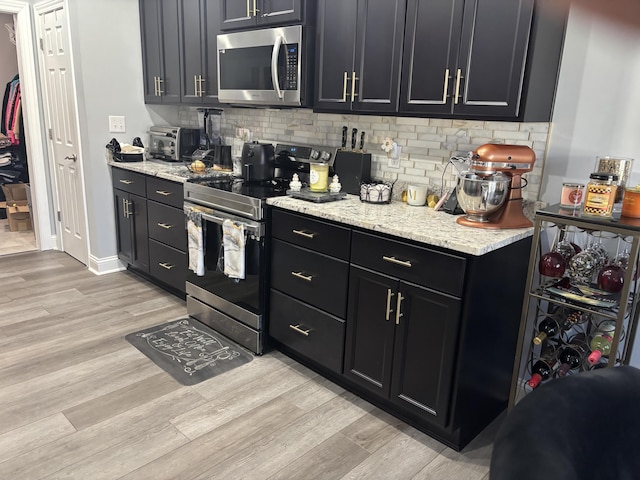 kitchen with light wood-style floors, dark cabinets, appliances with stainless steel finishes, and backsplash