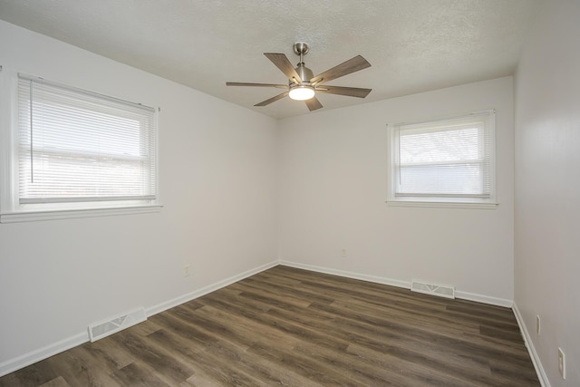 spare room with dark wood-type flooring, visible vents, a textured ceiling, and baseboards