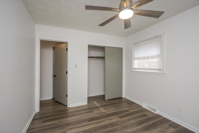 unfurnished bedroom with a textured ceiling, a closet, dark wood finished floors, and visible vents