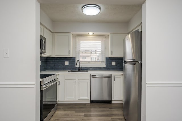 kitchen with appliances with stainless steel finishes, dark wood-style flooring, a sink, and white cabinetry