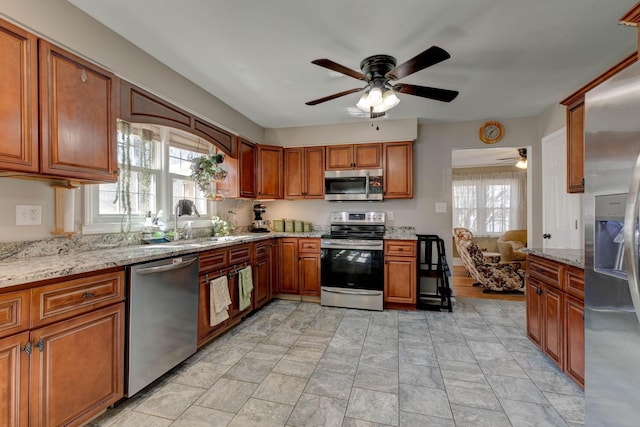 kitchen featuring stainless steel appliances, brown cabinets, a sink, and light stone counters