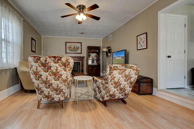 living area with visible vents, a ceiling fan, wood finished floors, and a glass covered fireplace