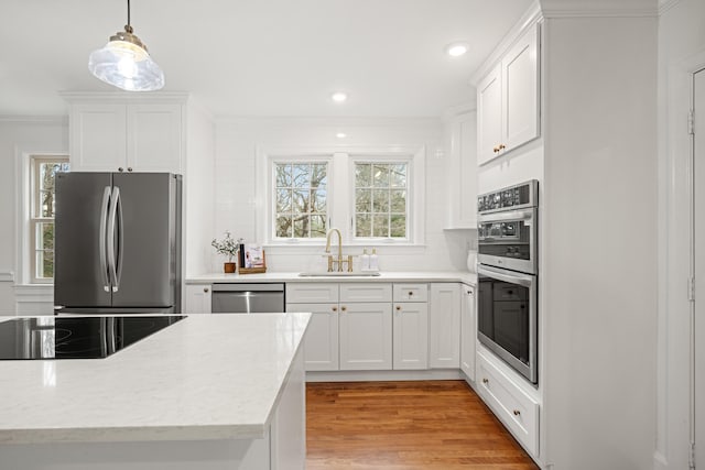 kitchen featuring stainless steel appliances, tasteful backsplash, ornamental molding, a sink, and light wood-type flooring