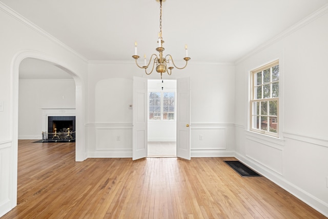 unfurnished dining area with visible vents, wood-type flooring, crown molding, a brick fireplace, and a chandelier