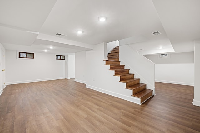 finished below grade area featuring stairs, wood finished floors, visible vents, and baseboards