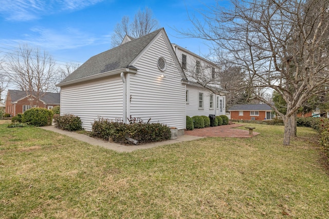 view of side of home with roof with shingles and a yard