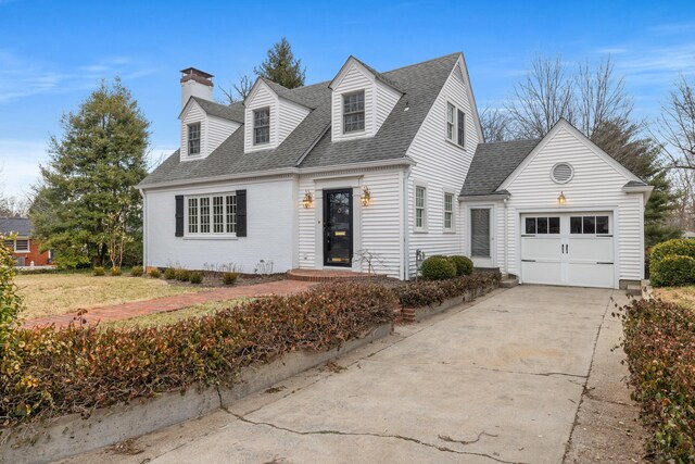 new england style home with roof with shingles, brick siding, a chimney, a garage, and driveway