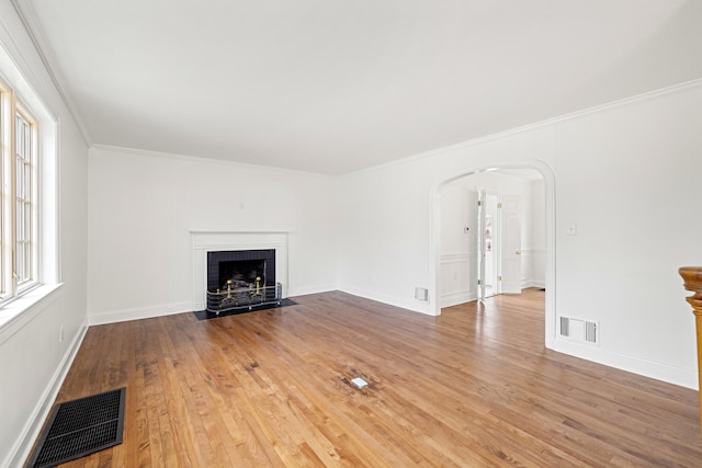 unfurnished living room featuring arched walkways, a brick fireplace, wood finished floors, and visible vents