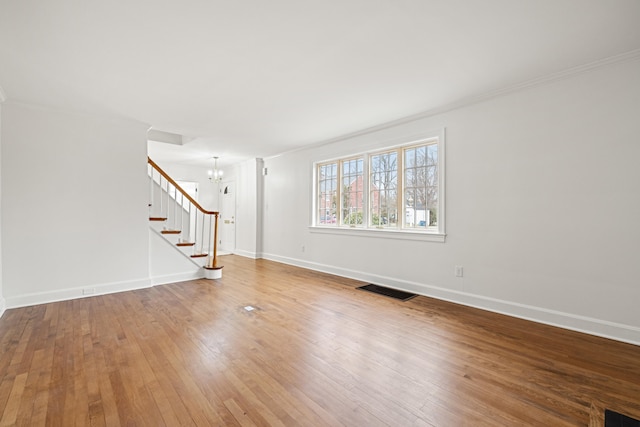 spare room featuring hardwood / wood-style flooring, visible vents, an inviting chandelier, baseboards, and stairs