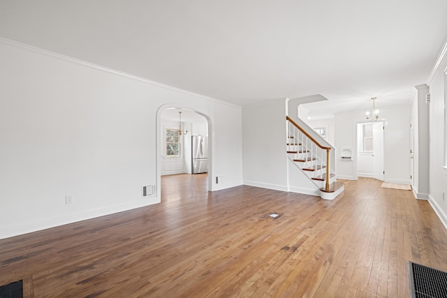 unfurnished living room featuring arched walkways, wood-type flooring, visible vents, a chandelier, and stairs