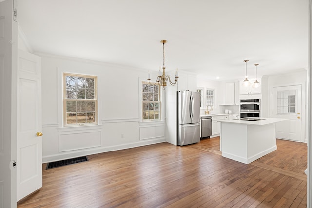 kitchen featuring visible vents, hardwood / wood-style floors, stainless steel appliances, light countertops, and white cabinetry