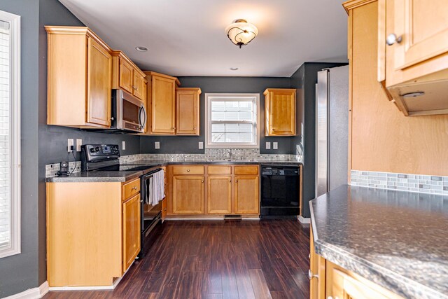 kitchen with a sink, baseboards, dark wood-style floors, black appliances, and dark countertops