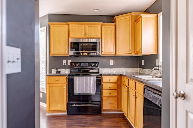 kitchen featuring baseboards, dark countertops, dark wood-type flooring, black appliances, and a sink