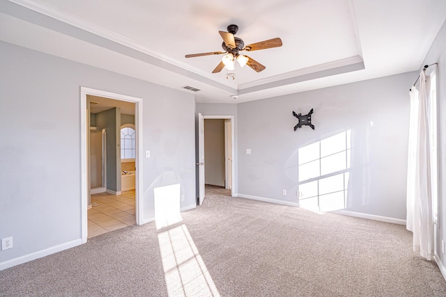 empty room with light colored carpet, a tray ceiling, visible vents, and baseboards