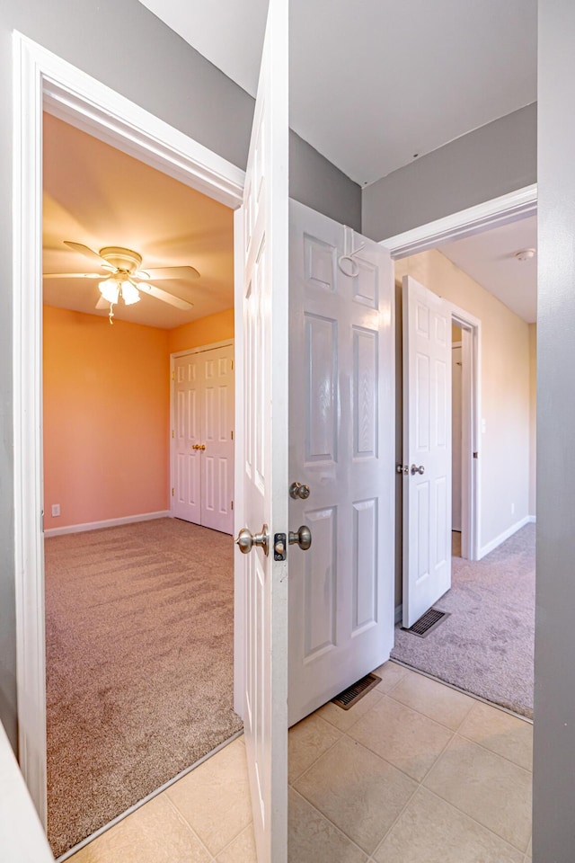 hallway featuring light carpet, baseboards, and light tile patterned flooring