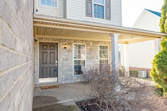 property entrance featuring covered porch, stone siding, and central AC unit