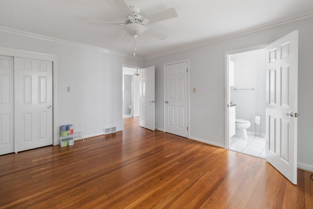 unfurnished bedroom with wood finished floors, visible vents, baseboards, ornamental molding, and ensuite bath