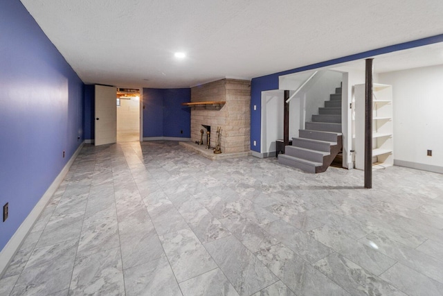 finished below grade area featuring stairs, baseboards, a textured ceiling, and a stone fireplace