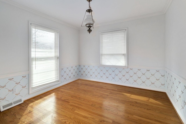 empty room featuring ornamental molding, a wainscoted wall, visible vents, and wood finished floors