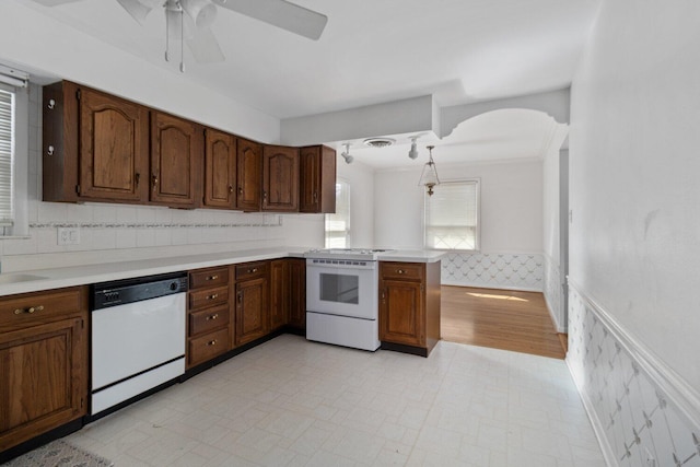 kitchen featuring white appliances, wainscoting, a peninsula, light countertops, and light floors