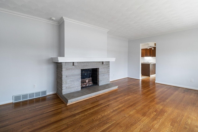 unfurnished living room featuring baseboards, visible vents, a fireplace with raised hearth, ornamental molding, and wood finished floors