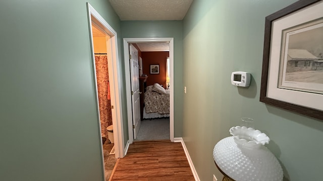 hall featuring baseboards, a textured ceiling, and wood finished floors