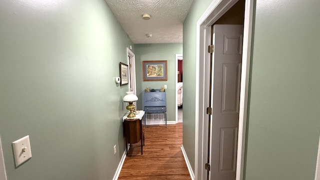 corridor with baseboards, a textured ceiling, and wood finished floors