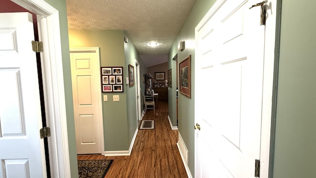 corridor with baseboards, visible vents, dark wood-type flooring, and a textured ceiling