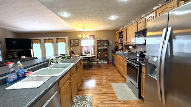 kitchen featuring a sink, appliances with stainless steel finishes, brown cabinets, light wood finished floors, and dark countertops