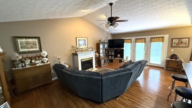 living area with lofted ceiling, a textured ceiling, wood finished floors, a ceiling fan, and a glass covered fireplace