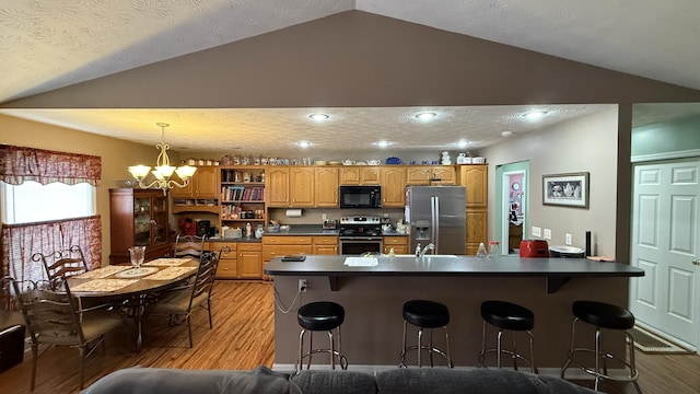 kitchen featuring stainless steel appliances, dark countertops, a peninsula, and light wood finished floors