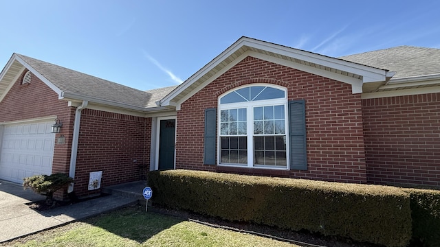 exterior space with an attached garage, roof with shingles, and brick siding